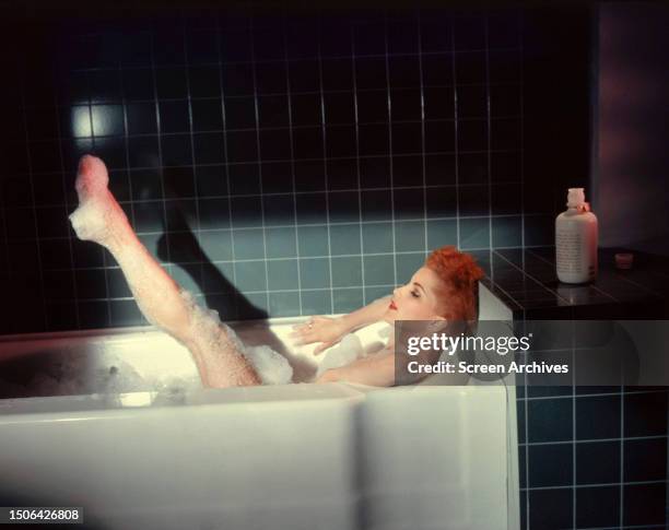 American actress Debra Paget with leg raised as she soaks in a bubble bath tub in a promotional still for the 1957 Thriller,' The River's Edge'.