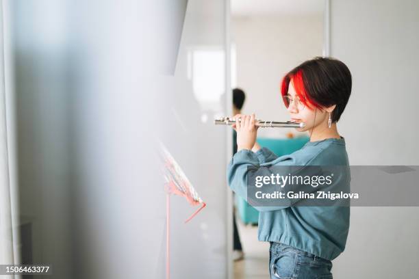 teenage girl with short haircut playing flute in children's room at home, child doing homework on music - flauto foto e immagini stock
