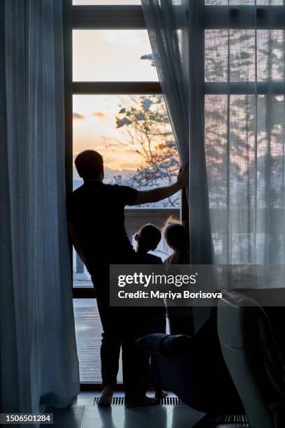 the family stands at the large panoramic window and looks at the sunset. - family trip in laws stock-fotos und bilder
