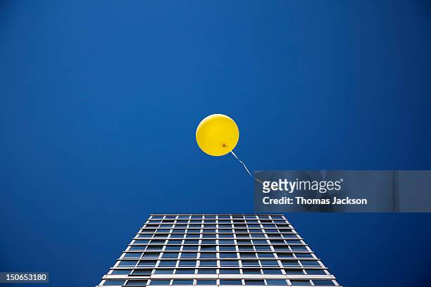 yellow balloon floating past single skyscraper - evasión fotografías e imágenes de stock