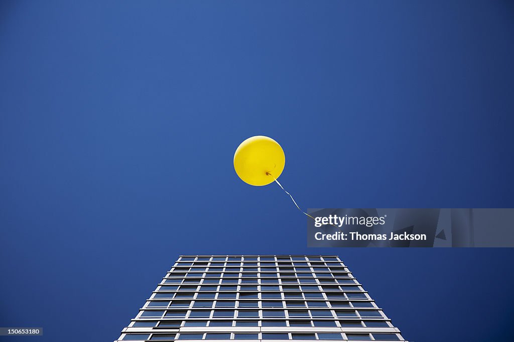 Yellow balloon floating past single skyscraper