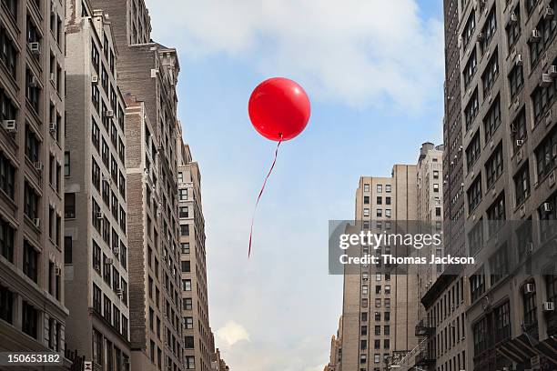 red balloon floating through city - ballon de baudruche photos et images de collection