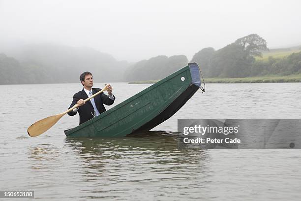 man in suit paddling unbalanced boat - sinking stockfoto's en -beelden