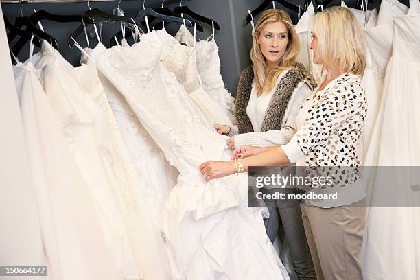 mother and daughter looking at each other while selecting wedding gown in bridal store - wedding dress store stock pictures, royalty-free photos & images