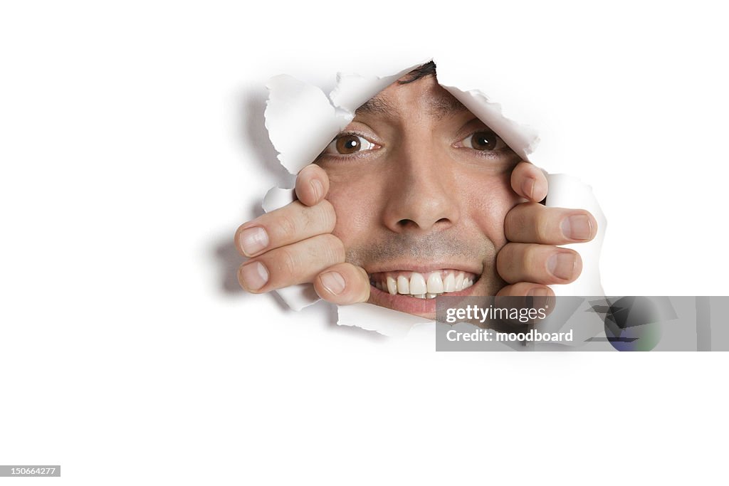 Portrait of a happy young Hispanic man peeking from ripped paper hole