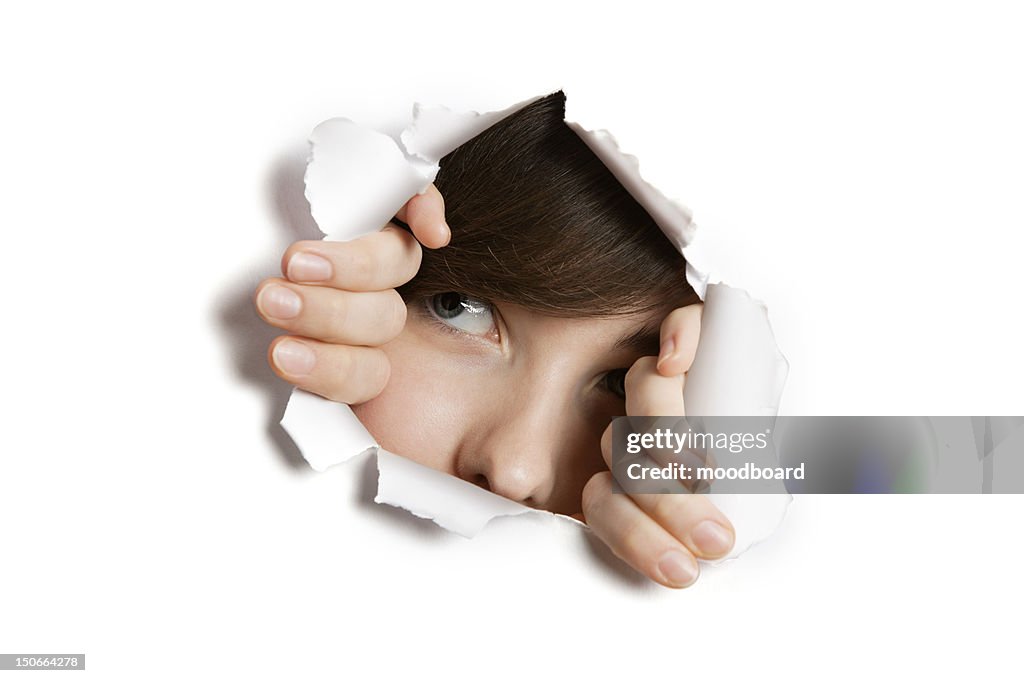 Young Middle eastern woman peeking from ripped white paper hole