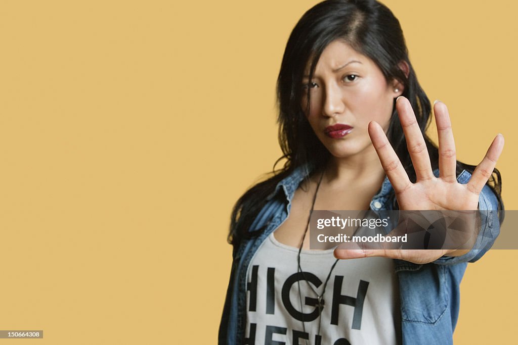 Portrait of a young woman gesturing stop sign over colored background