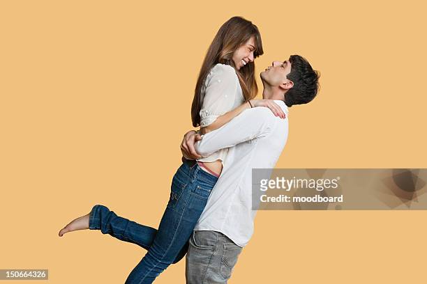side view of young couple looking at each other while man carrying girlfriend over colored background - couple in love stock pictures, royalty-free photos & images