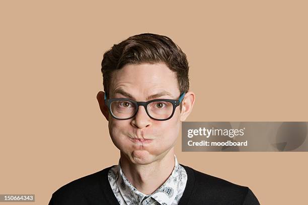 portrait of mid adult man puffing cheeks over colored background - man expressive background glasses stock-fotos und bilder