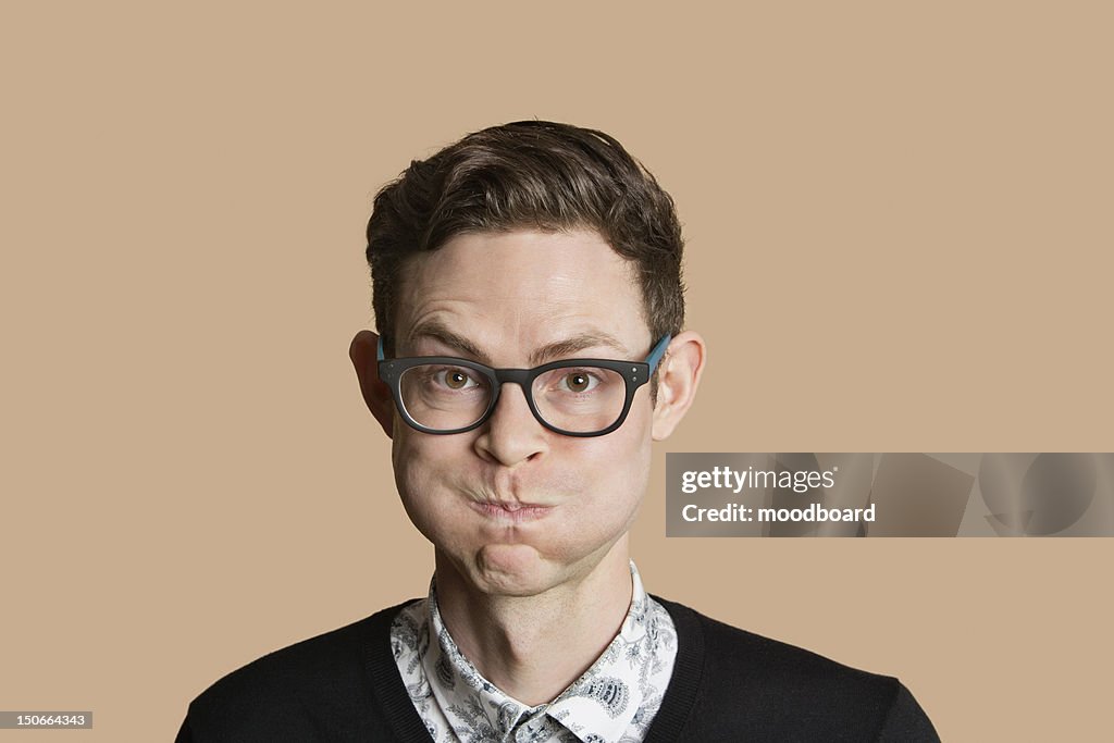 Portrait of mid adult man puffing cheeks over colored background