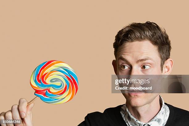 mid adult man looking at lollipop over colored background - a361 stock pictures, royalty-free photos & images