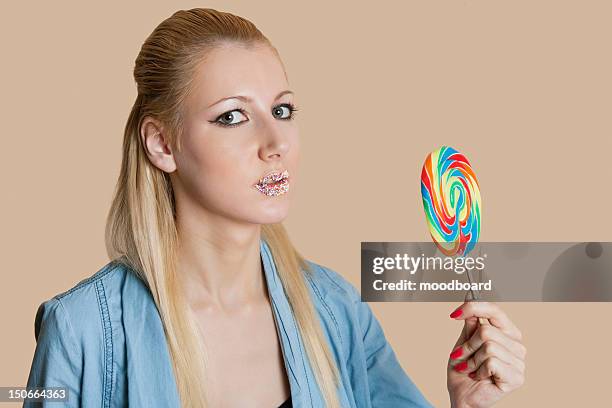 portrait of a blond woman with sprinkled lips holding lollipop over colored background - candy lips stock pictures, royalty-free photos & images