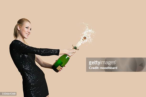 beautiful young woman uncorking champagne bottle over colored background - woman holding champagne stock-fotos und bilder