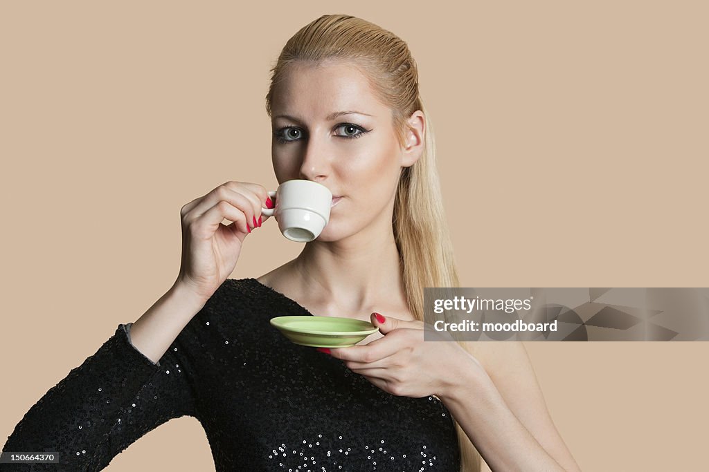 Portrait of beautiful young woman drinking tea over colored background