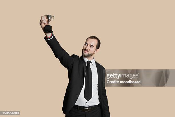 happy young man raising winning trophy over colored background - people holding trophy stock pictures, royalty-free photos & images