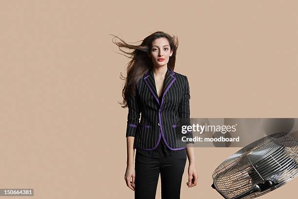 portrait of a beautiful woman standing while fan blowing her hair over colored background - schwarzes haar stock-fotos und bilder