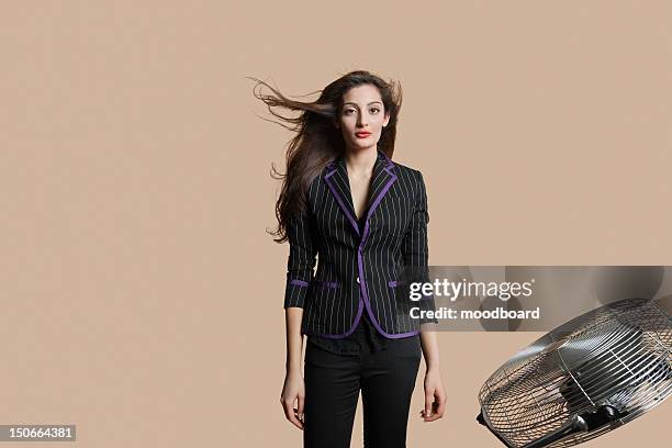 portrait of a beautiful woman standing while fan blowing her hair over colored background - black hair bildbanksfoton och bilder