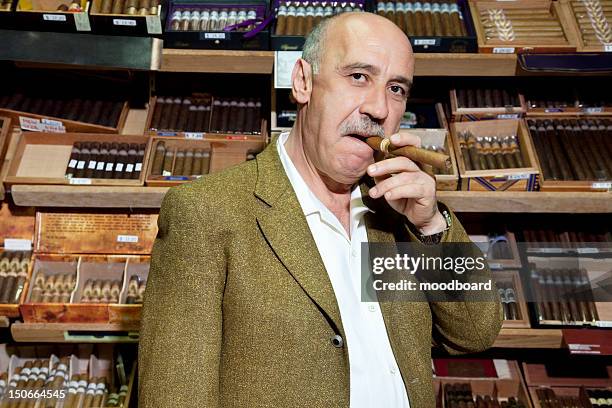 portrait of mature tobacco shop owner smoking cigar in store - tobacconists stock pictures, royalty-free photos & images