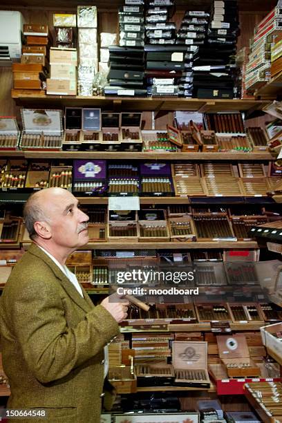 mature tobacco shop owner looking at cigars on display - tobacconists stock pictures, royalty-free photos & images