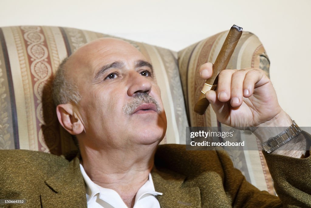 Mature man smoking cigar while relaxing on armchair