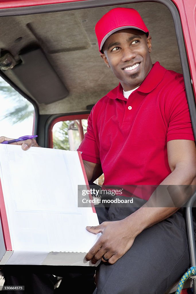 Young African American man sitting in delivery truck with box