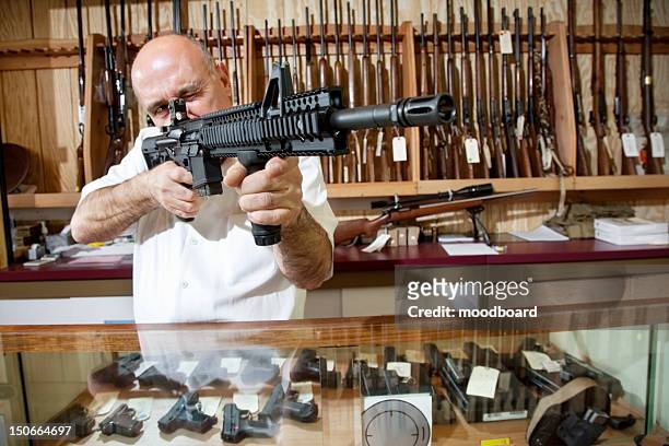 mature merchant aiming with rifle in gun shop - weapon foto e immagini stock