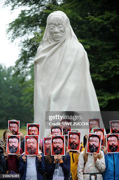 Young visitors of the dOCUMENTA fair for contemporary art pose with portraits of Chinese artist Ai Weiwei in front of the ghost statue by Thai artist...