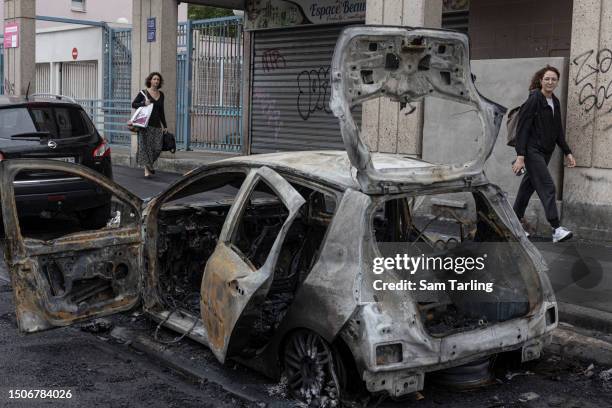 Passerby looks at the scorched remains of a car that was set on fire during a fourth night of unrest on the outskirts of Paris, on July 1, 2023 in...