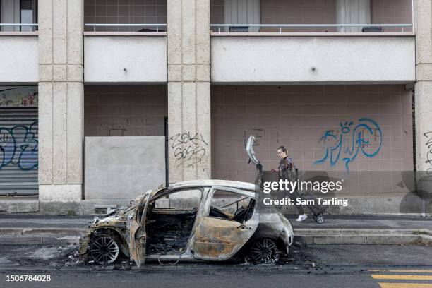 Passerby looks at the scorched remains of a car that was set on fire during a fourth night of unrest on the outskirts of Paris, on July 1, 2023 in...