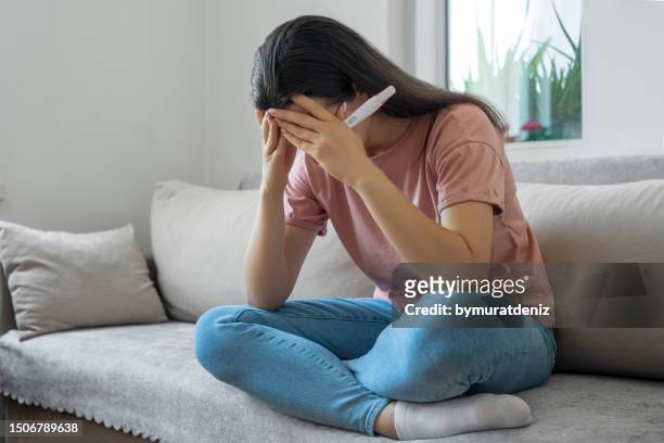 sad woman sitting on sofa and holding pregnancy test with negative result - artificial insemination stock pictures, royalty-free photos & images