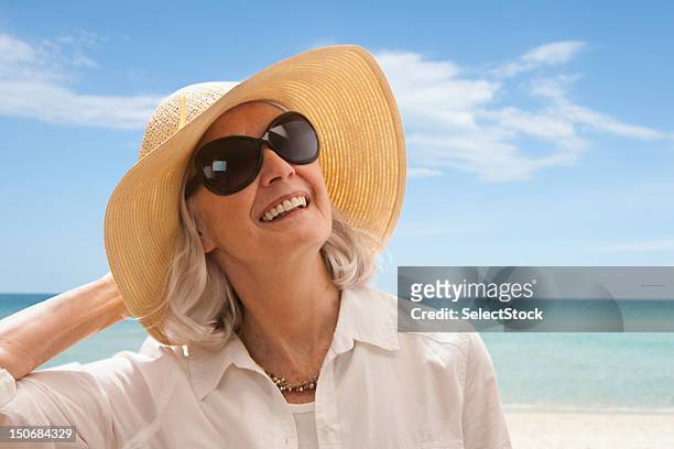 senior woman on beach holding hat - sun hat stock pictures, royalty-free photos & images