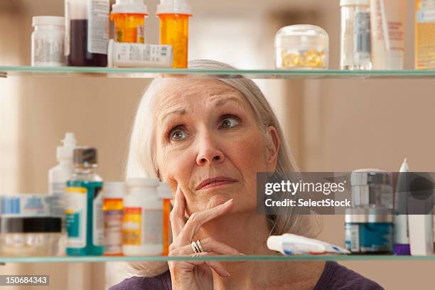 senior woman looking through medicine cabinet - bathroom cabinet stock pictures, royalty-free photos & images