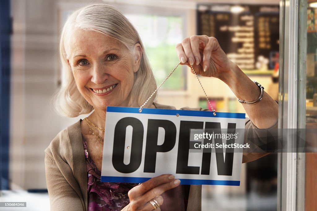 Senior woman holding up open sign