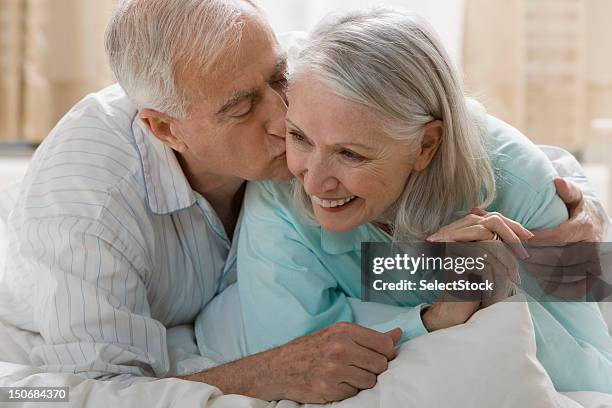 senior man kissing wife in bed - falling in love stock pictures, royalty-free photos & images