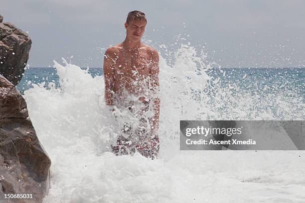 young man braces against pounding surf, by rock - brown hair waves stock pictures, royalty-free photos & images