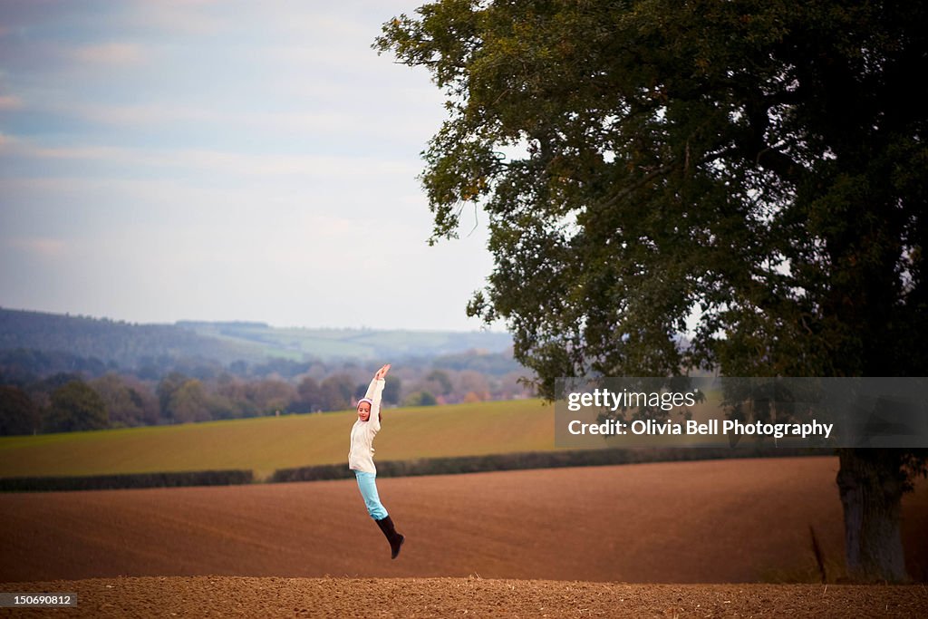 Girl jumping on Ploughed Field in autumn