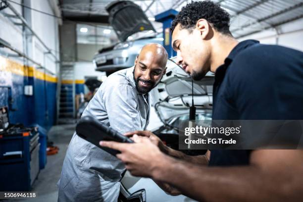 mechaniker unterhalten sich bei der reparatur eines autos in einer autowerkstatt - automechaniker stock-fotos und bilder