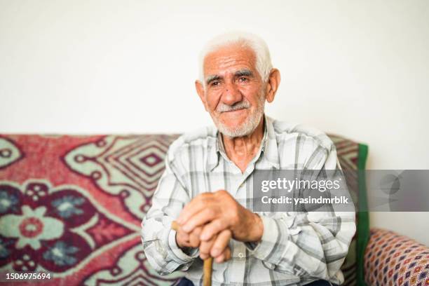 white haired senior man sitting on sofa holding walking stick - turkse etniciteit stockfoto's en -beelden