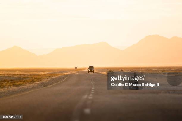car driving on desert road at sunset - wüstenstraße stock-fotos und bilder