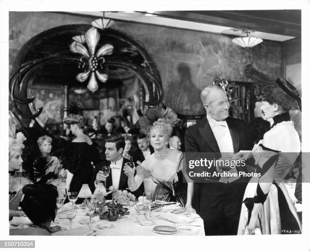 Louis Jourdan, Eva Gabor, and Maurice Chevalier in packed dining room in a scene from the film 'Gigi', 1958.