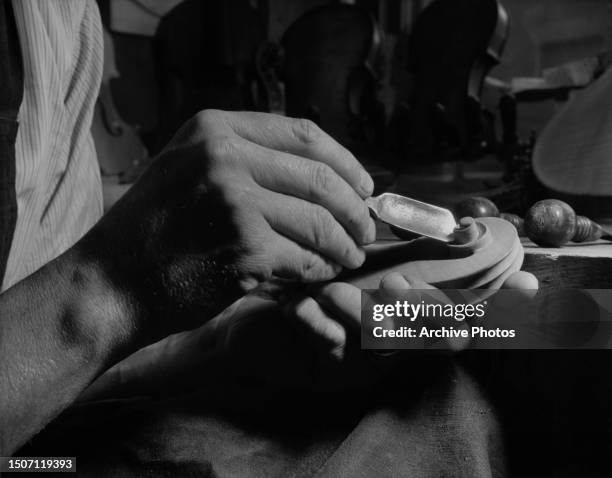 Close-up view of British-German luthier Paul Voight using a violin-makers knife to shape the scroll, the curled embellishment at the top of the neck,...