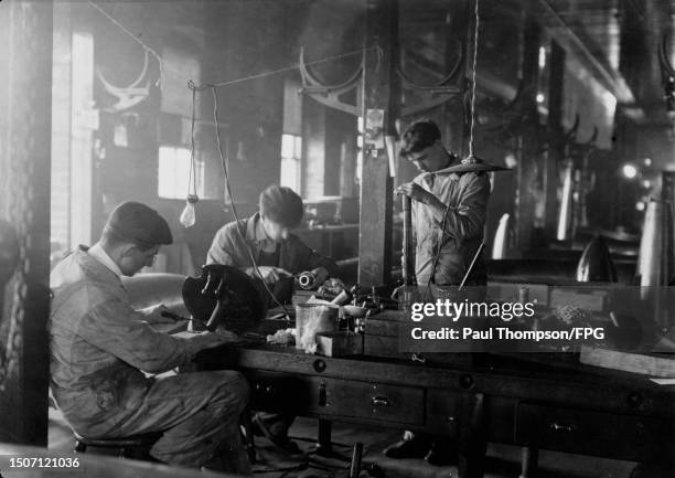 Munitions workers around a workbench making primers in a munitions factory, United States, circa 1935. A primer initiates the combustion that enables...