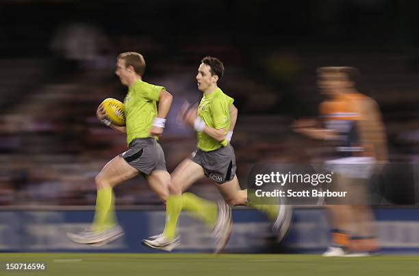 The referees run with the ball to the centre circle after a goal during the round 22 AFL match between the St Kilda Saints and the Greater Western...