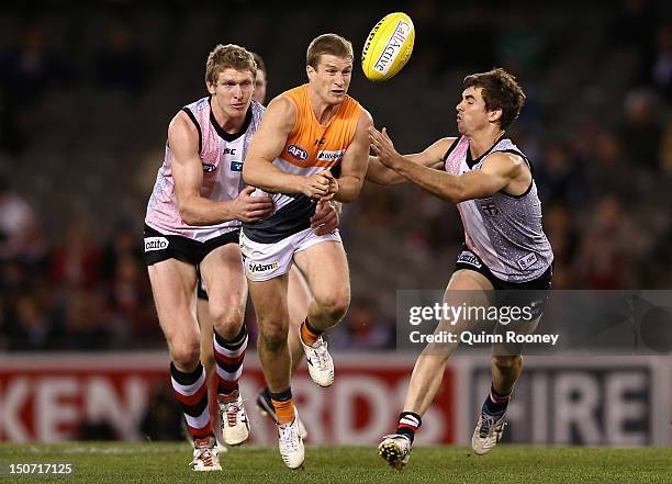 Luke Power of the Giants handballs whilst being tackled by Ben McEvoy of the Saints during the round 22 AFL match between the St Kilda Saints and the...