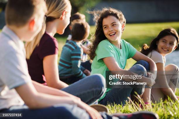 gruppe von kindern, die auf dem gras sitzen und sich in der natur unterhalten - group of children stock-fotos und bilder