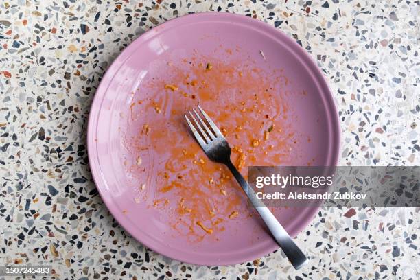 a dirty empty plate and fork on a wooden kitchen or dining table. cutlery is used, symbolizing the end of lunch or dinner. a portion of food eaten, overeating. - leerer teller stock-fotos und bilder