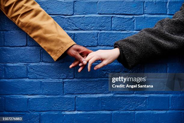 love united: multiracial couple holding hands against blue wall - kindness stock pictures, royalty-free photos & images