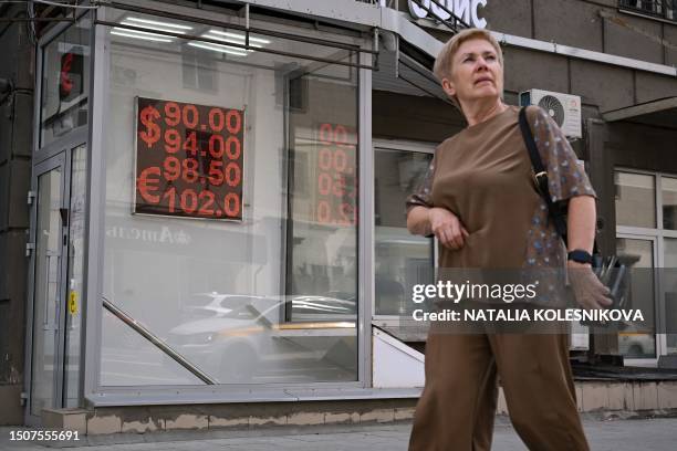 Woman walks past a board showing currency exchange rates of the US dollar and the euro against the Russian ruble in Moscow on July 6 as the Russian...