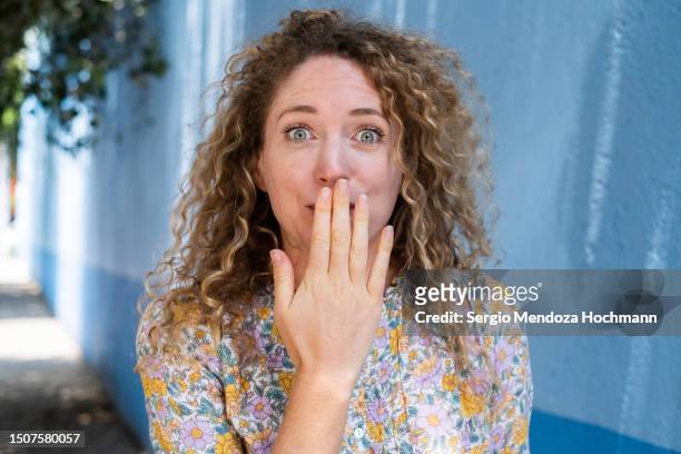 young woman with curly blonde hair covering her mouth with an oops gesture, whoops, error, mistake, speak no evil - dumb blonde stock pictures, royalty-free photos & images