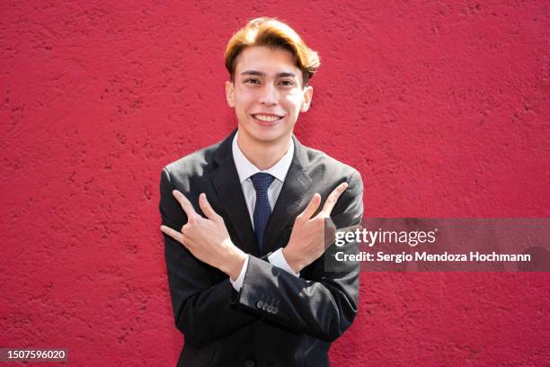 young latino man in a suit and tie looking at the camera and doing the heavy metal horns hand sign - heavy metal horns stock pictures, royalty-free photos & images